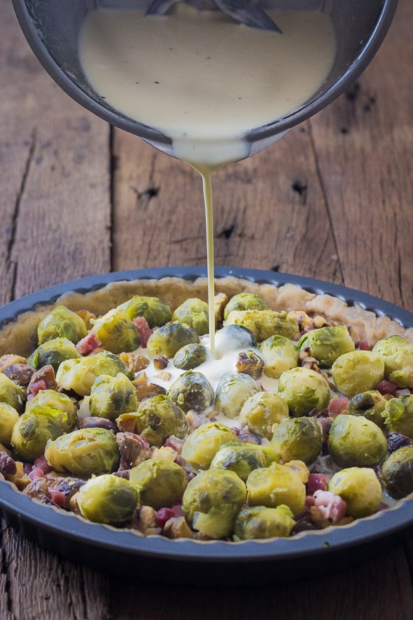 pouring filling into the brusses sprouts quiche quiche